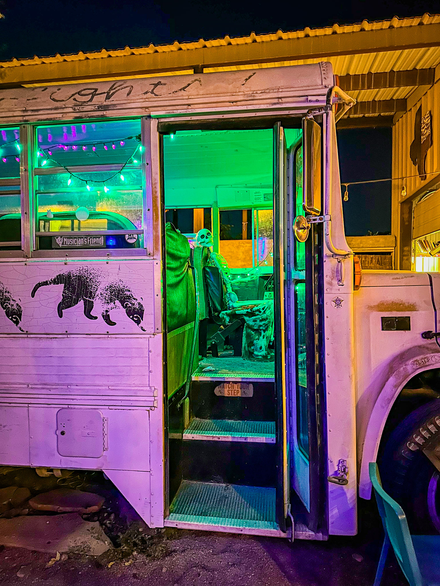 A converted bus illuminated by ethereal green and purple lights, featuring street art and a skeleton decoration